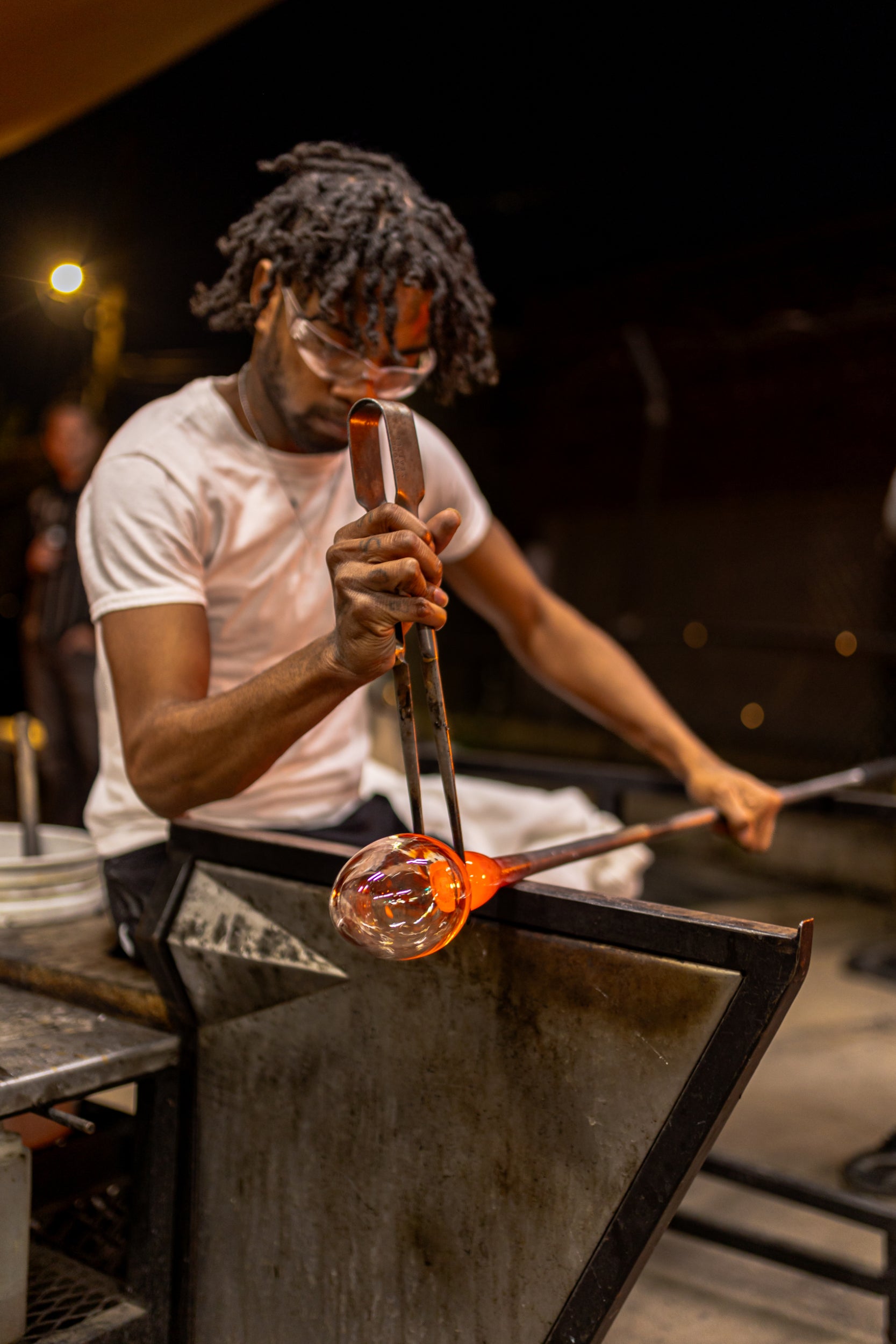 Glassblower shaping molten glass with tools in a workshop setting